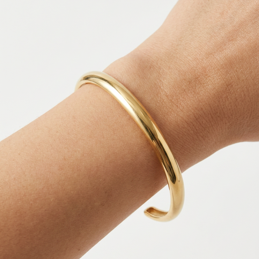 Gold bracelet on a wrist against a light gray background