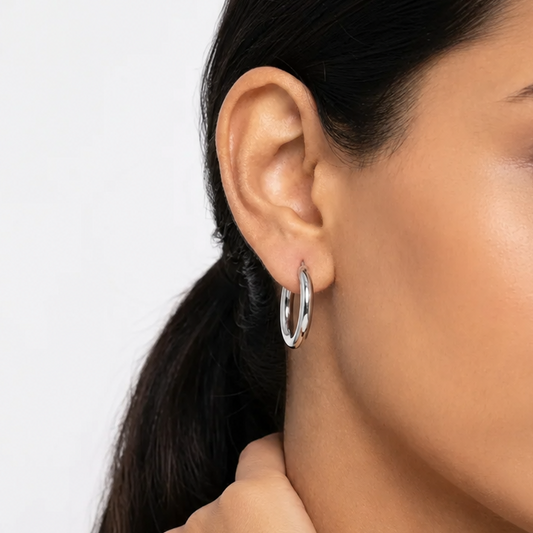 Close-up of a woman wearing silver hoop earrings with a neutral background