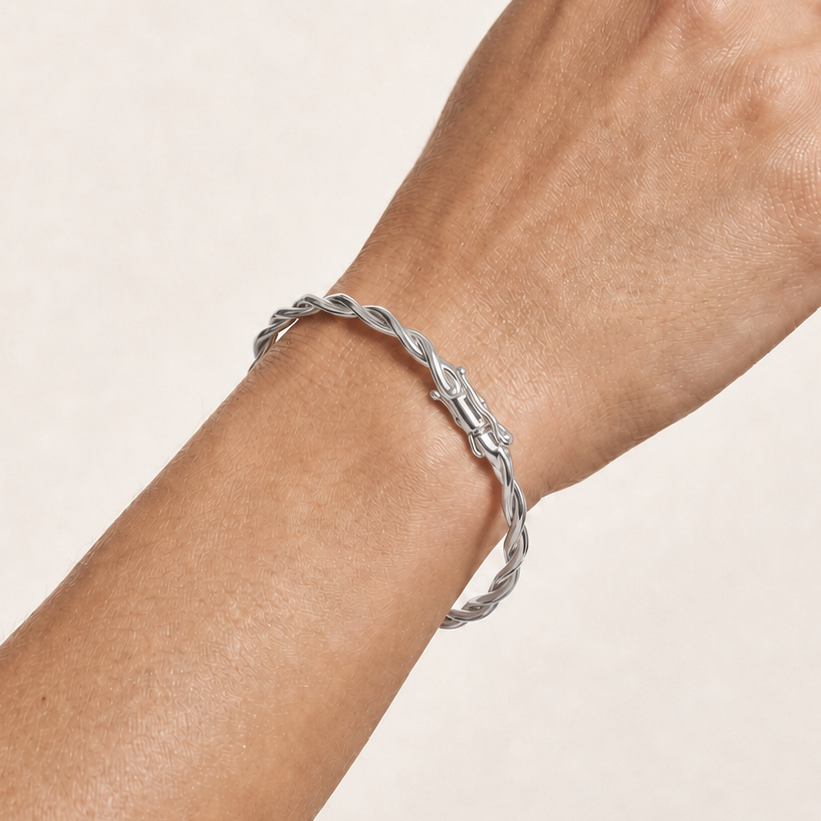 A close-up of a person's hand and wrist wearing a twisted silver bangle bracelet against a light beige background.