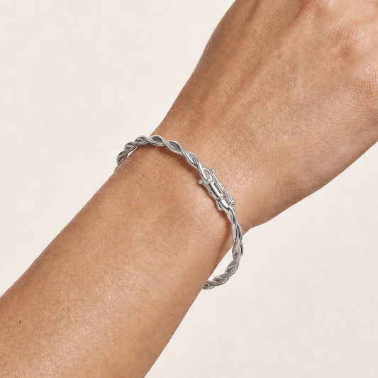 A close-up of a person's hand and wrist wearing a twisted silver bangle bracelet against a light beige background.