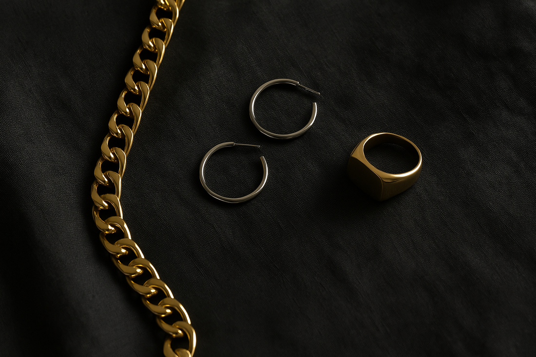 Flat lay of solid 18k gold jewellery including a chunky gold chain, minimalist white gold hoops, and a gold signet ring on a dark textured linen surface, photographed in soft natural light.