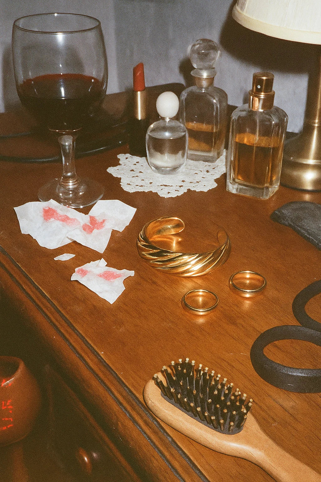Wooden surface with various items including a glass of red wine, perfume bottles, and grooming tools.