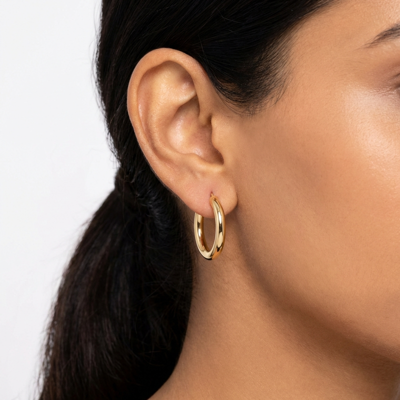 Close-up of a person wearing a gold hoop earring on a plain background