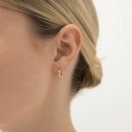 Gold hoop earring worn by a person with blonde hair on a white background